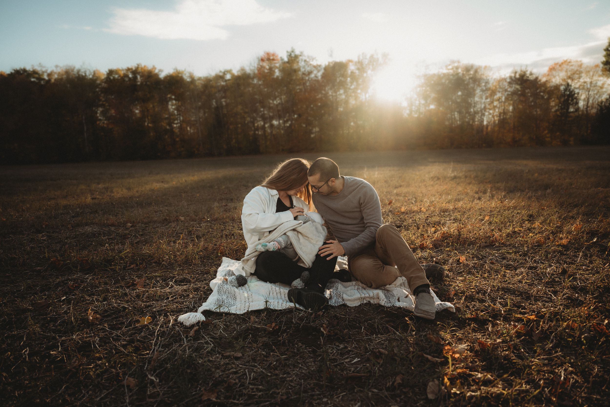 Family shares tender moment together on blanket in sunlit autumn field.
