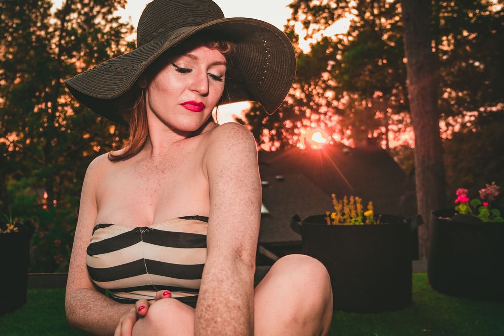 Vintage-inspired photo of model in striped swimsuit and wide hat at sunset.
