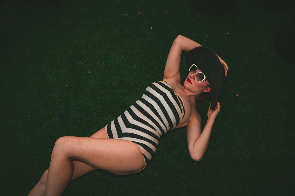 Artistic photo of model in striped swimsuit reclining on dark background.