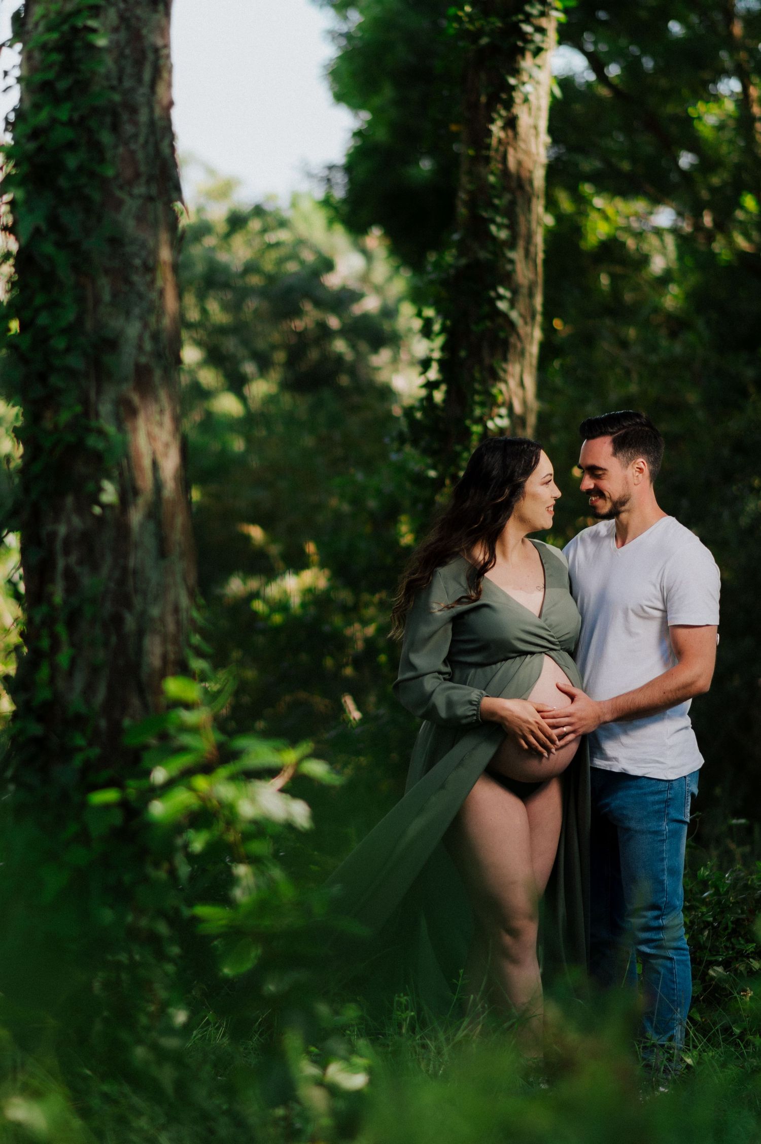 Romantic maternity photo of couple in lush forest setting.