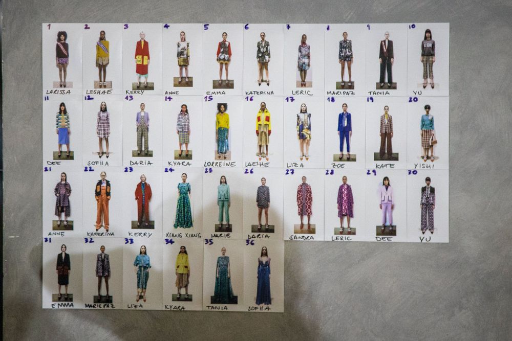 A grid display showing 30 different fashion outfit designs and sketches on a gray wall.