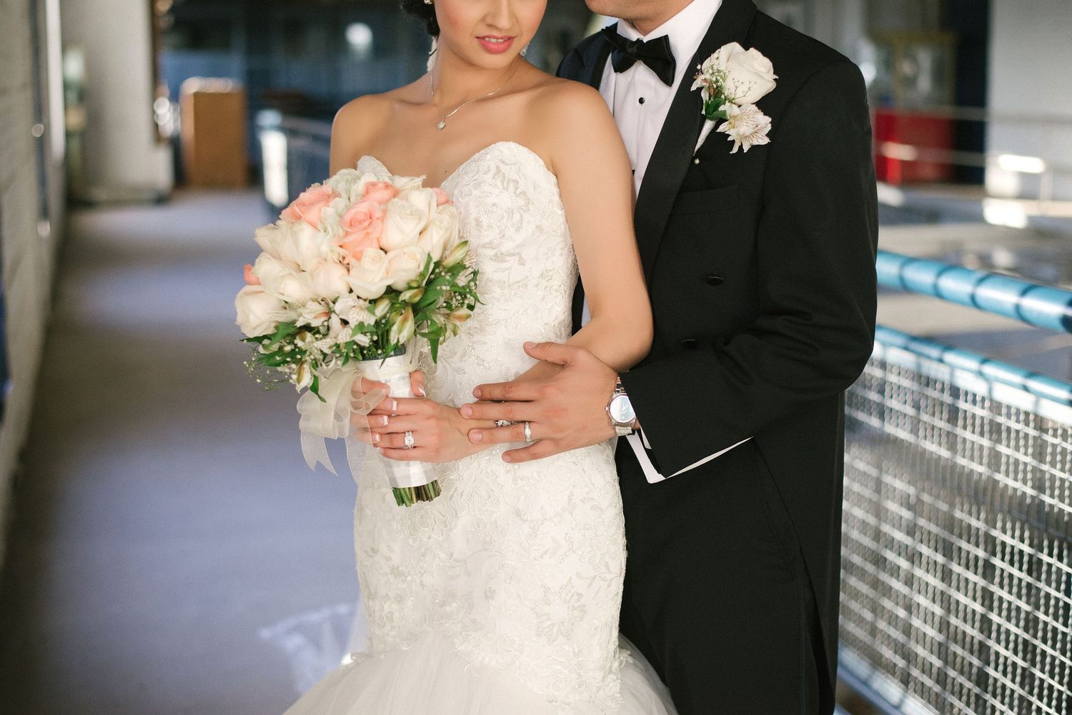 Elegant couple in formal wedding attire posing against modern tile background.