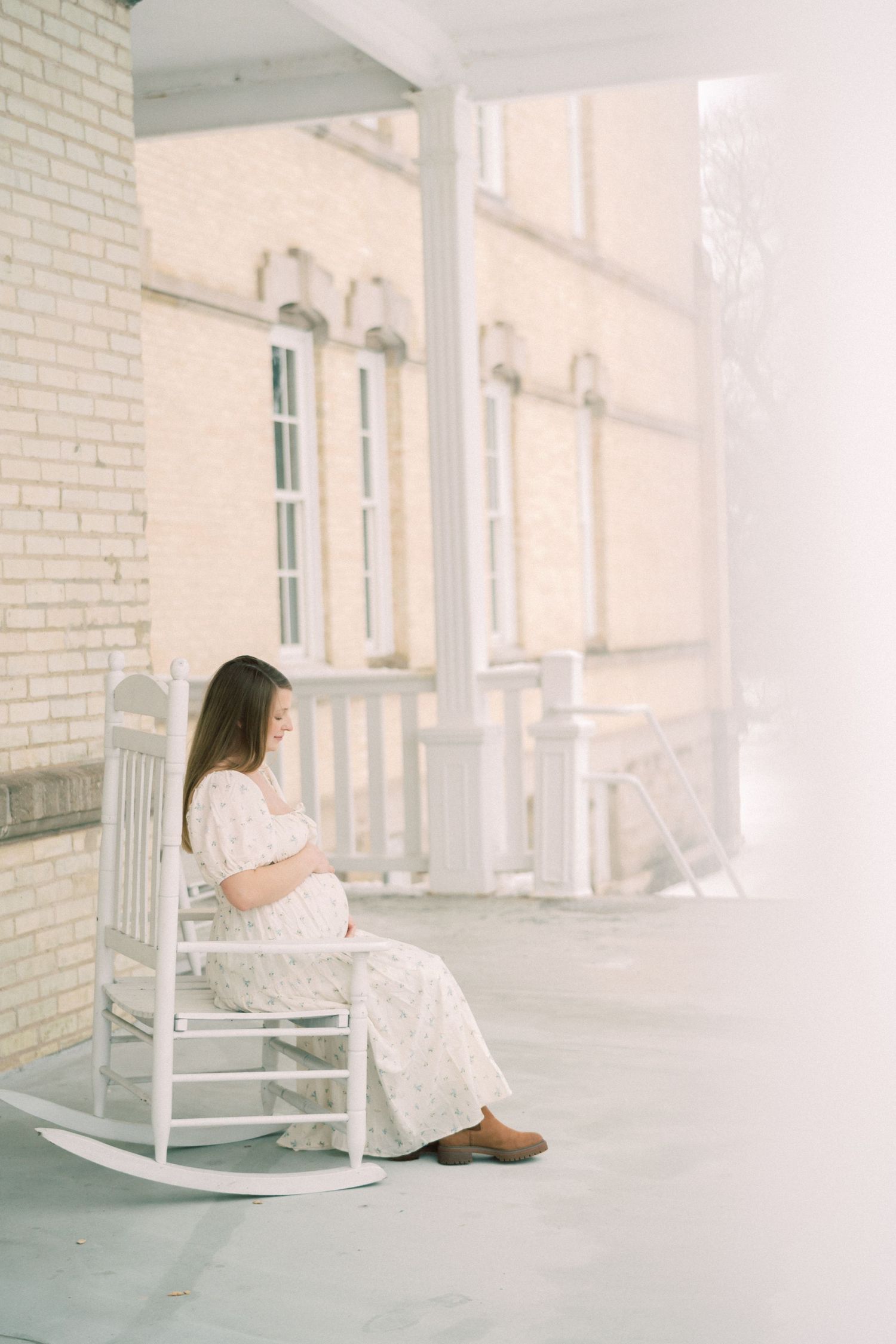 A rocking chair sits on a bright white porch with vintage arched windows and classical architectural details in the background.