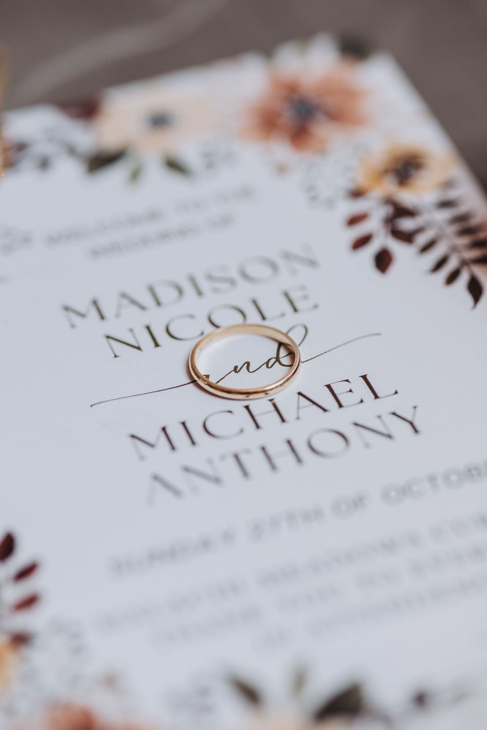 Elegant wedding invitation with gold ring and floral details showing names Madison Nicole and Michael Anthony.