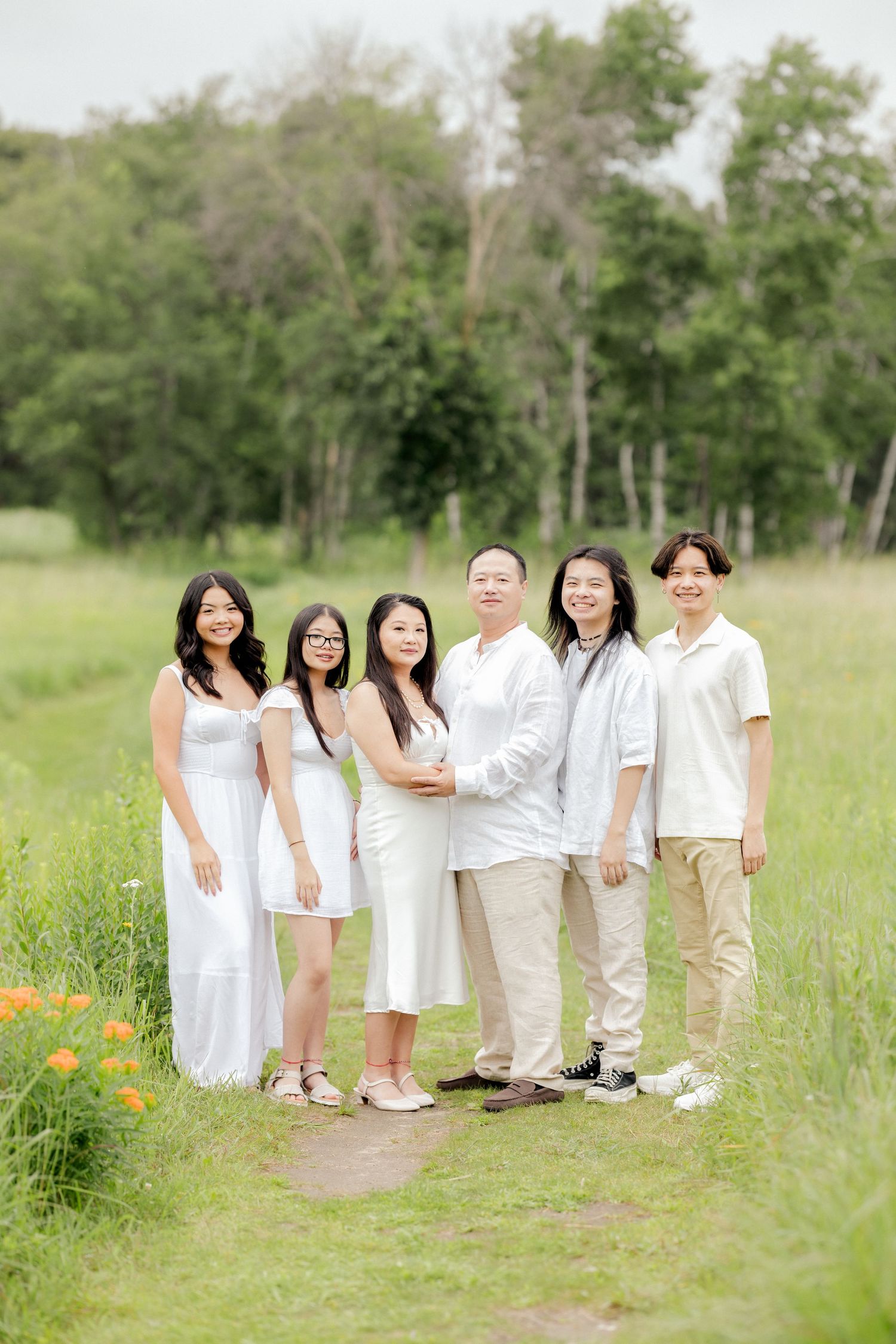 Family group portrait in coordinated white and cream outfits standing in a grassy field.