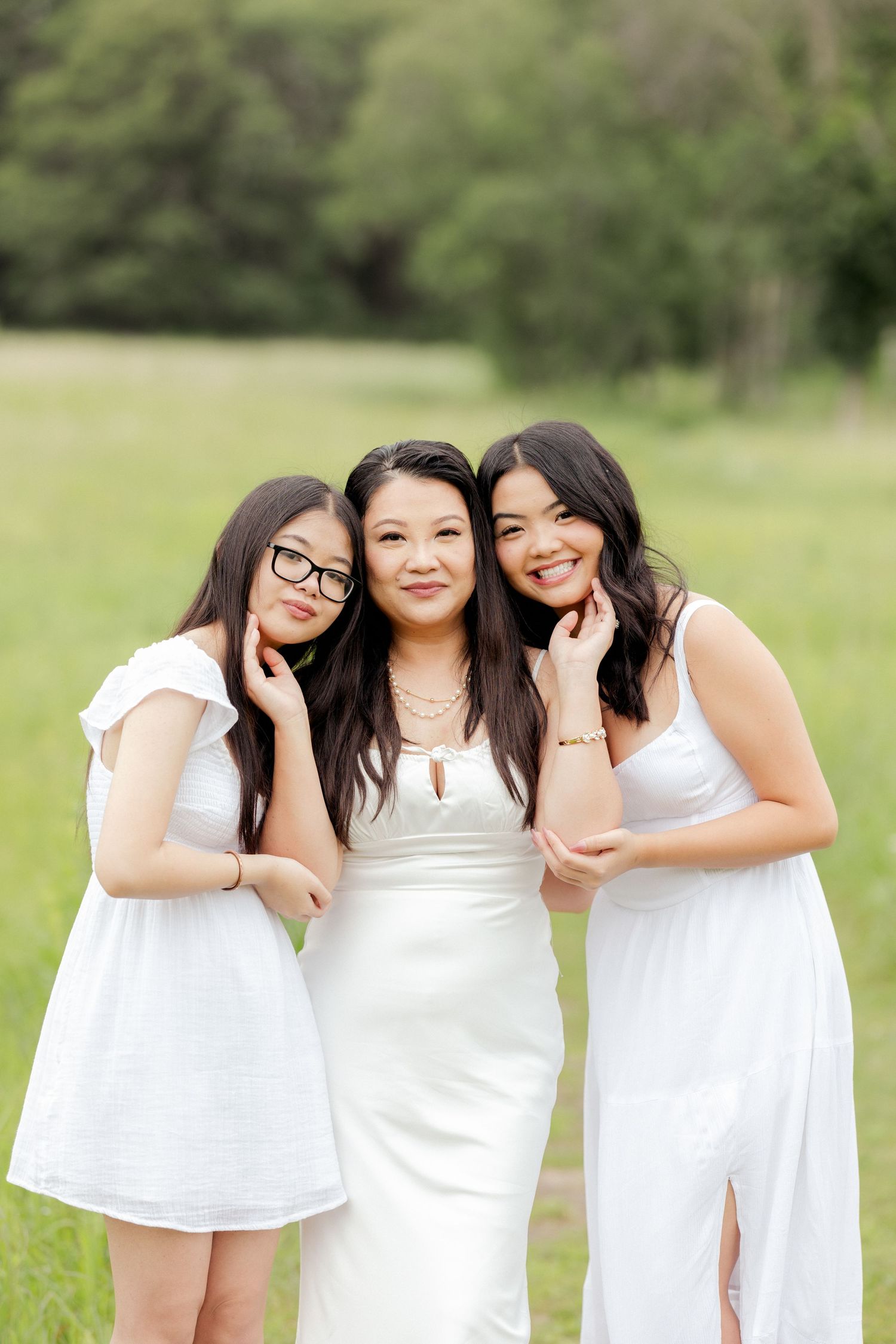 Three women in coordinated white dresses pose together on a grassy field.