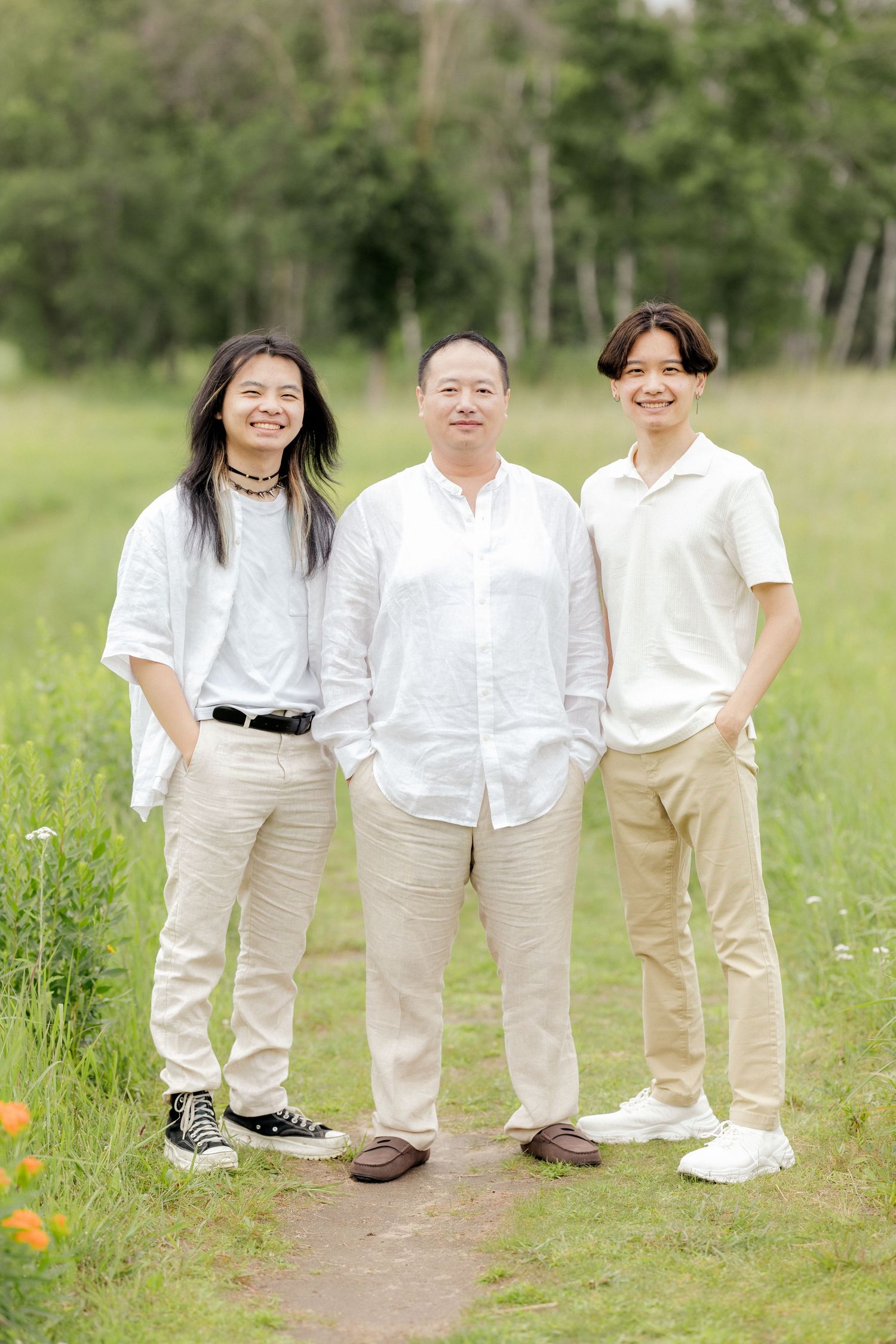 Three people in white and beige outfits stand together on a dirt path.