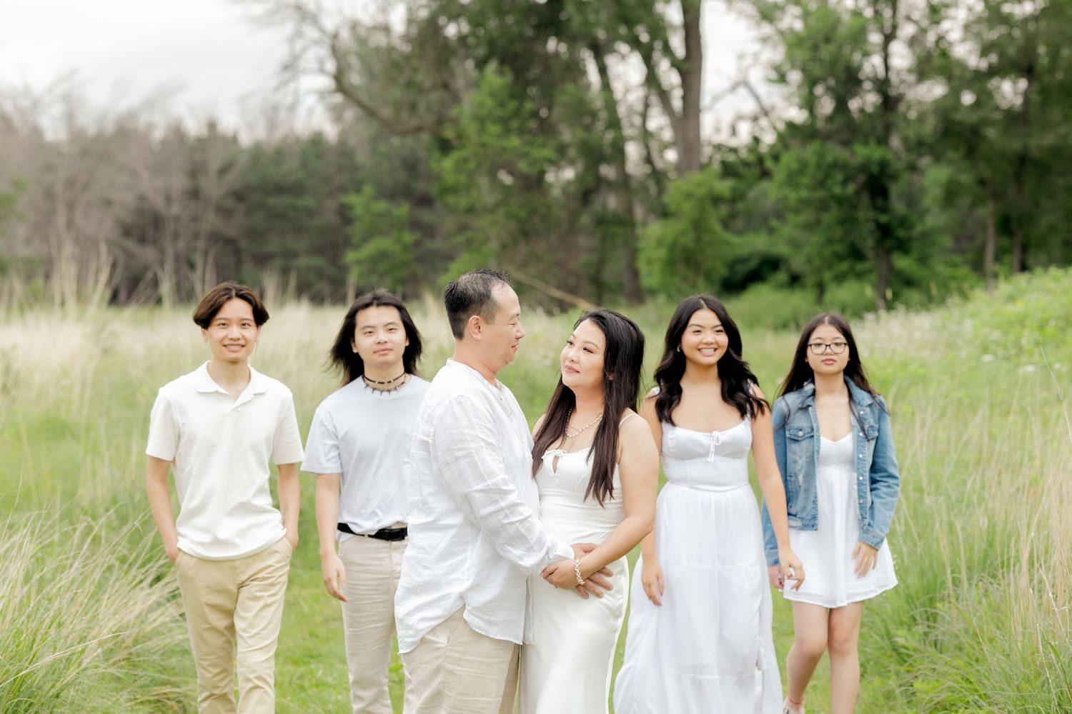 A group poses together in a sunlit field wearing coordinated white and light-colored outfits.