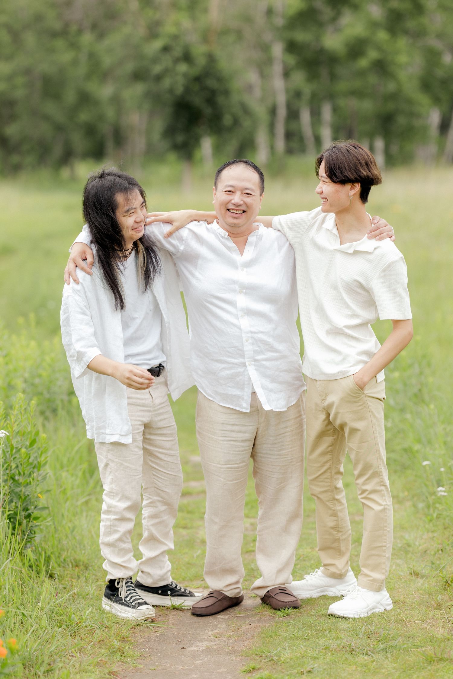 Three people in light colored clothing share a candid moment outdoors.