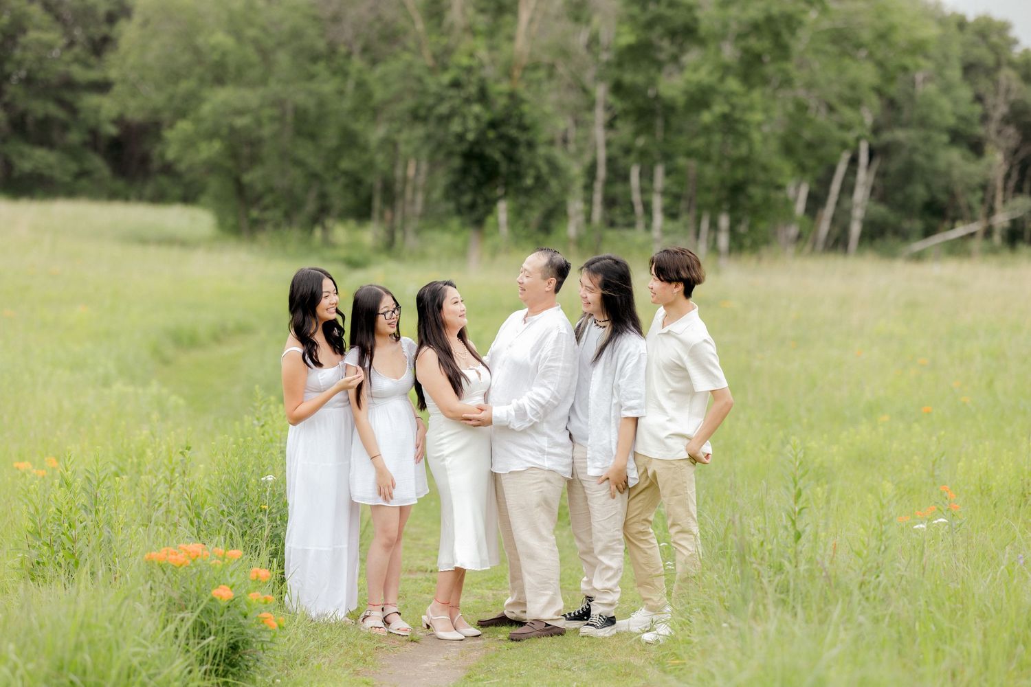 Family members in white and cream outfits chatting together in a scenic meadow.