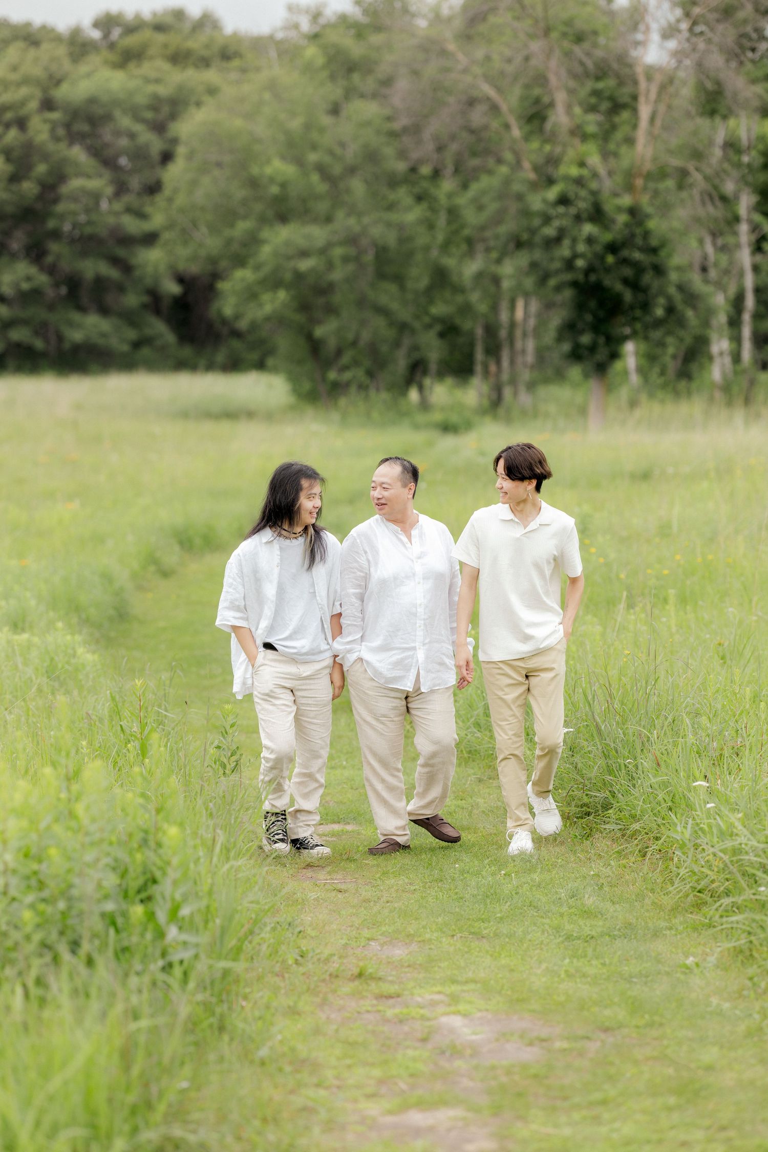 Three people in coordinating white and beige outfits walk along a nature path.
