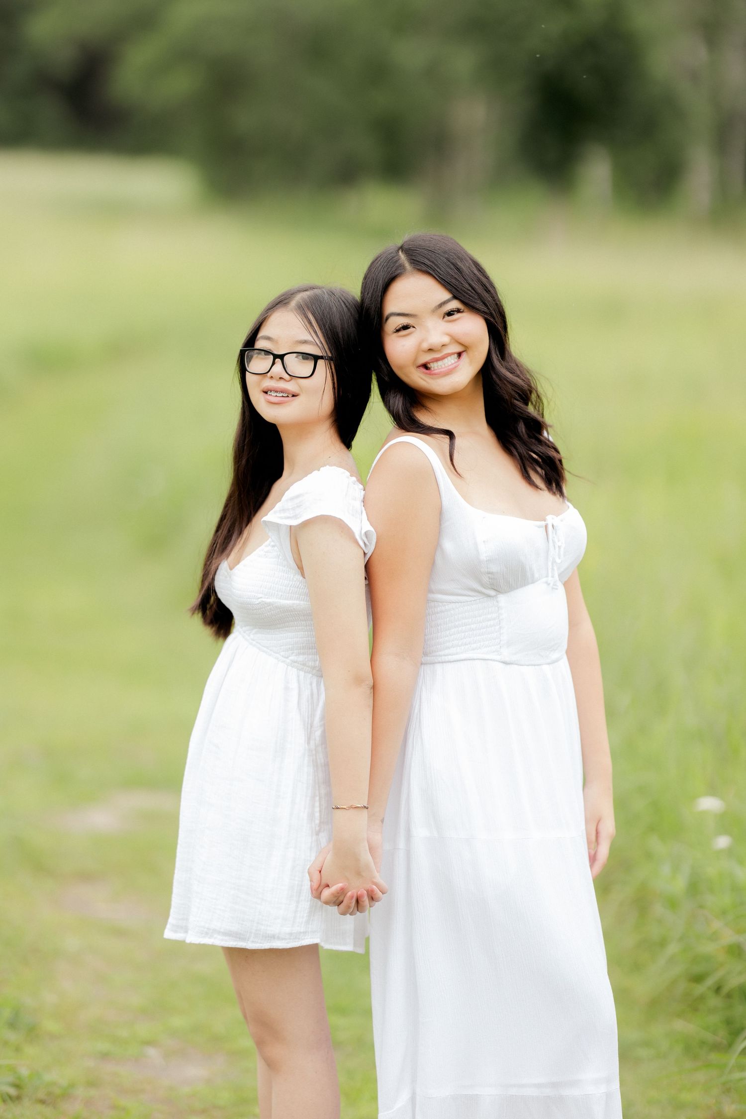 Two women in white dresses pose together in a sunny meadow.