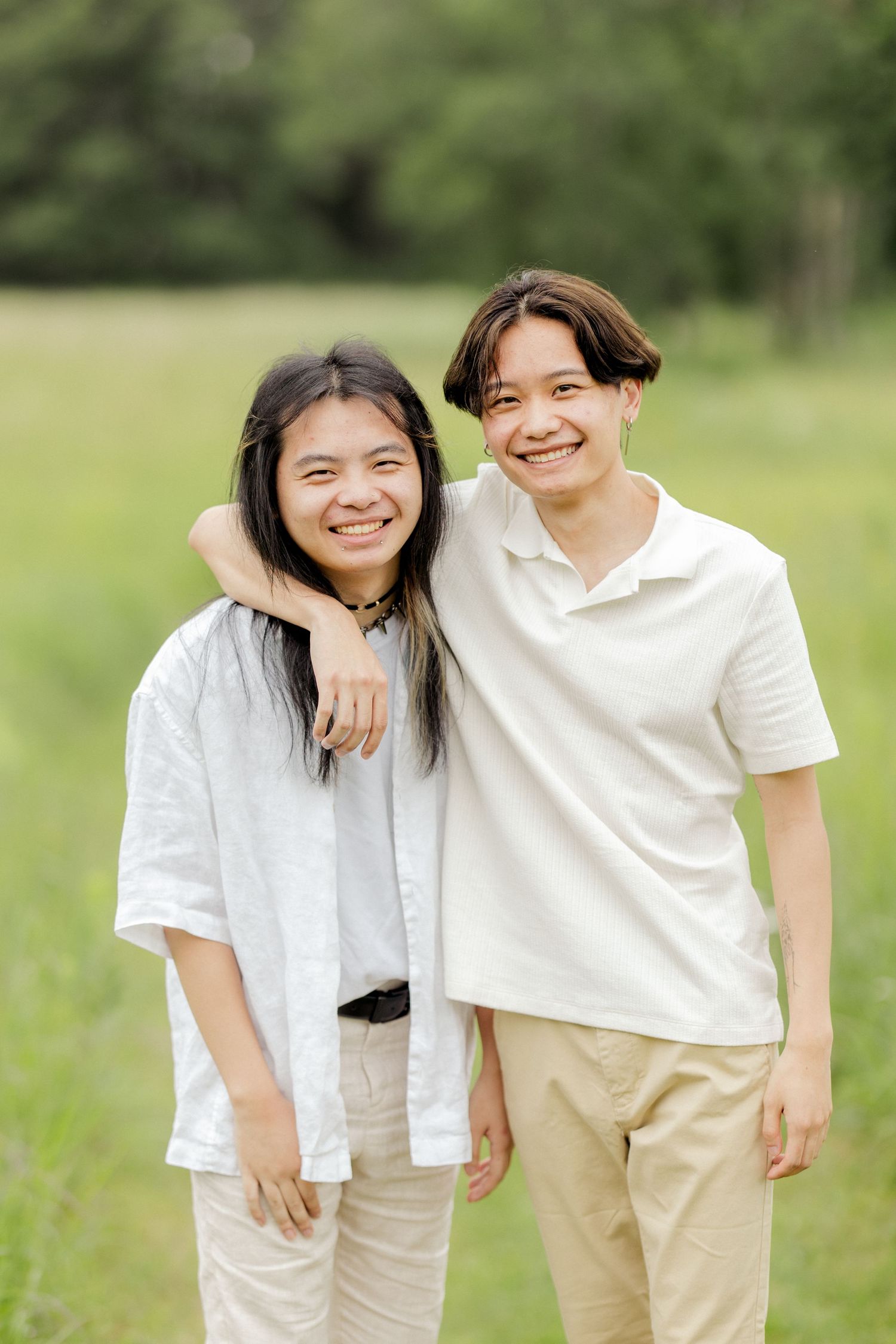 Two people in casual white outfits embrace while standing in a green field.