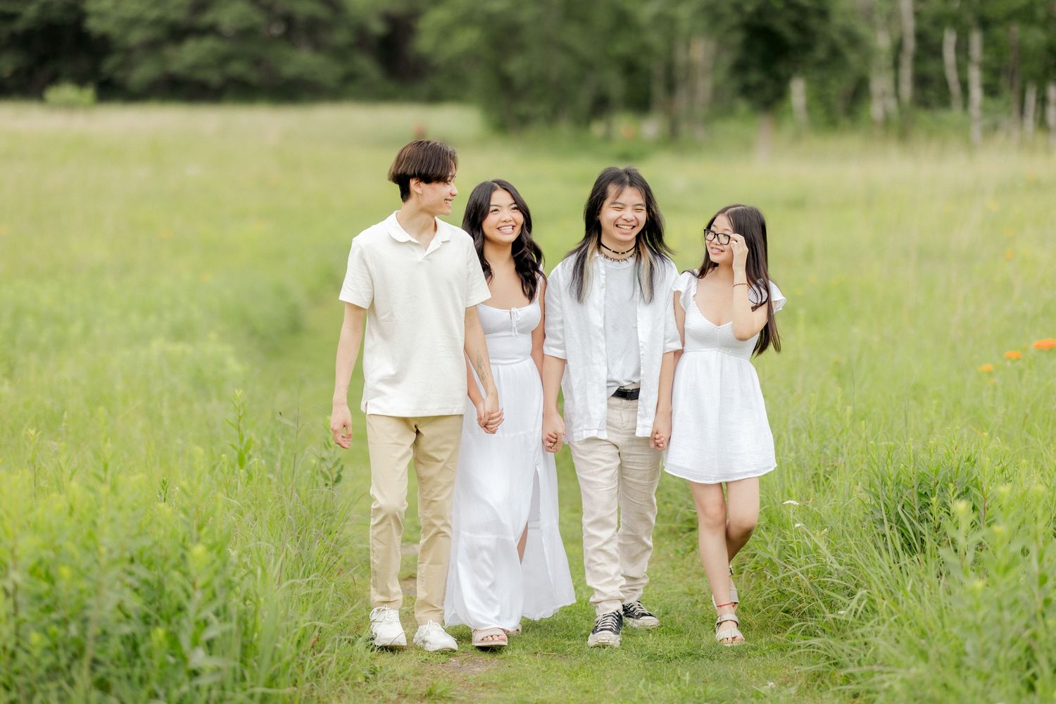Four people in white and beige outfits walking together through tall grass.
