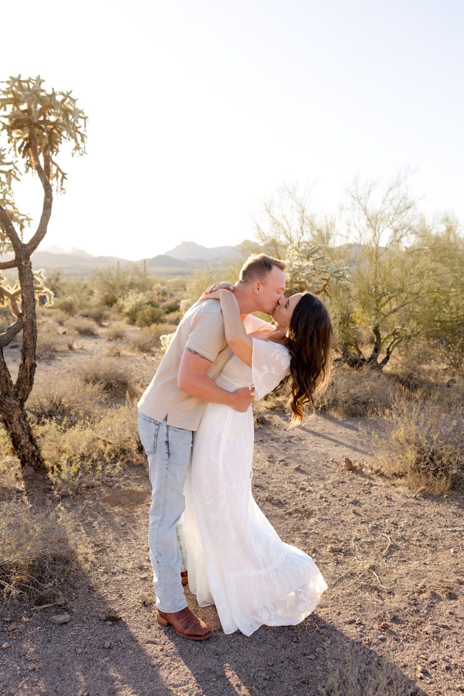 A romantic photoshoot of a couple sharing tender moments together in a desert setting during golden hour sunset.