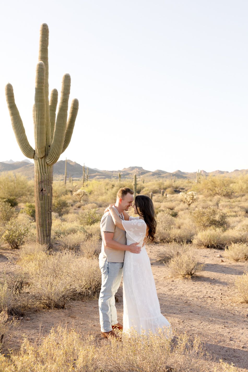 Couple embraces in the Arizona desert surrounded by towering saguaro cacti at sunset.