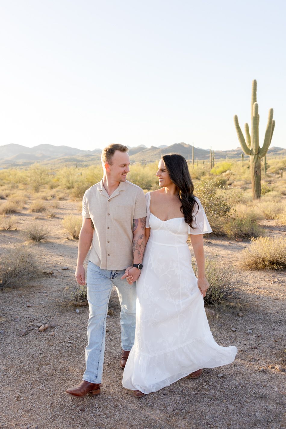 A couple enjoys an intimate moment together in a picturesque desert landscape with towering saguaro cacti.
