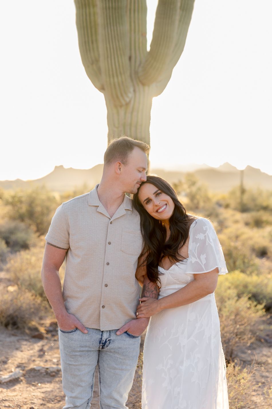 A couple embraces and laughs together in the desert during sunset with a saguaro cactus in the background.