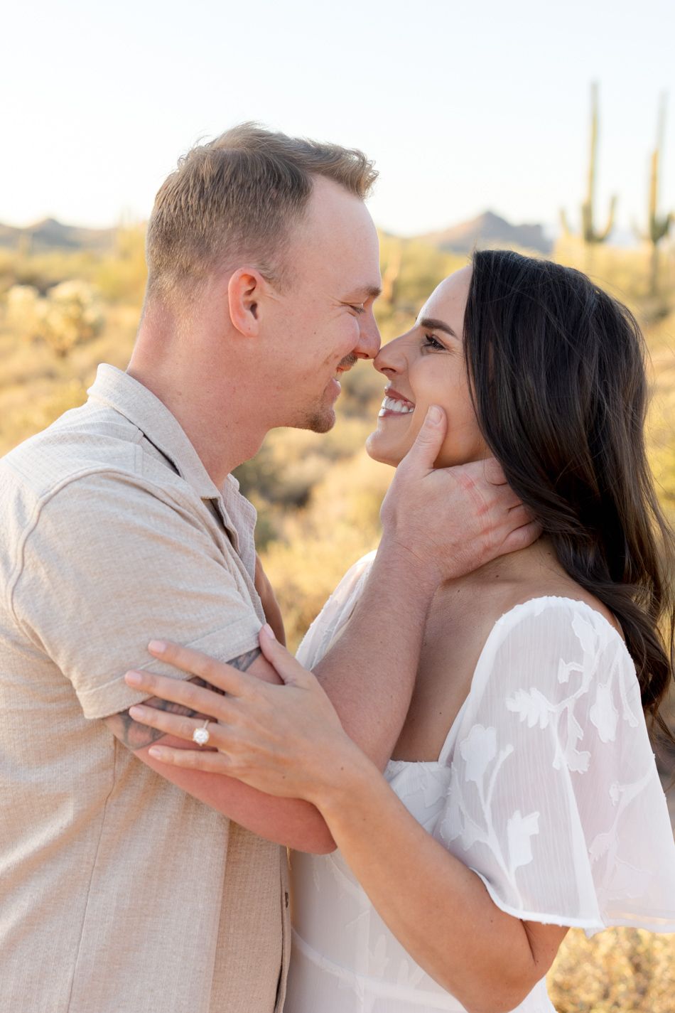 A romantic couple embraces in a desert landscape with saguaro cacti at golden hour.