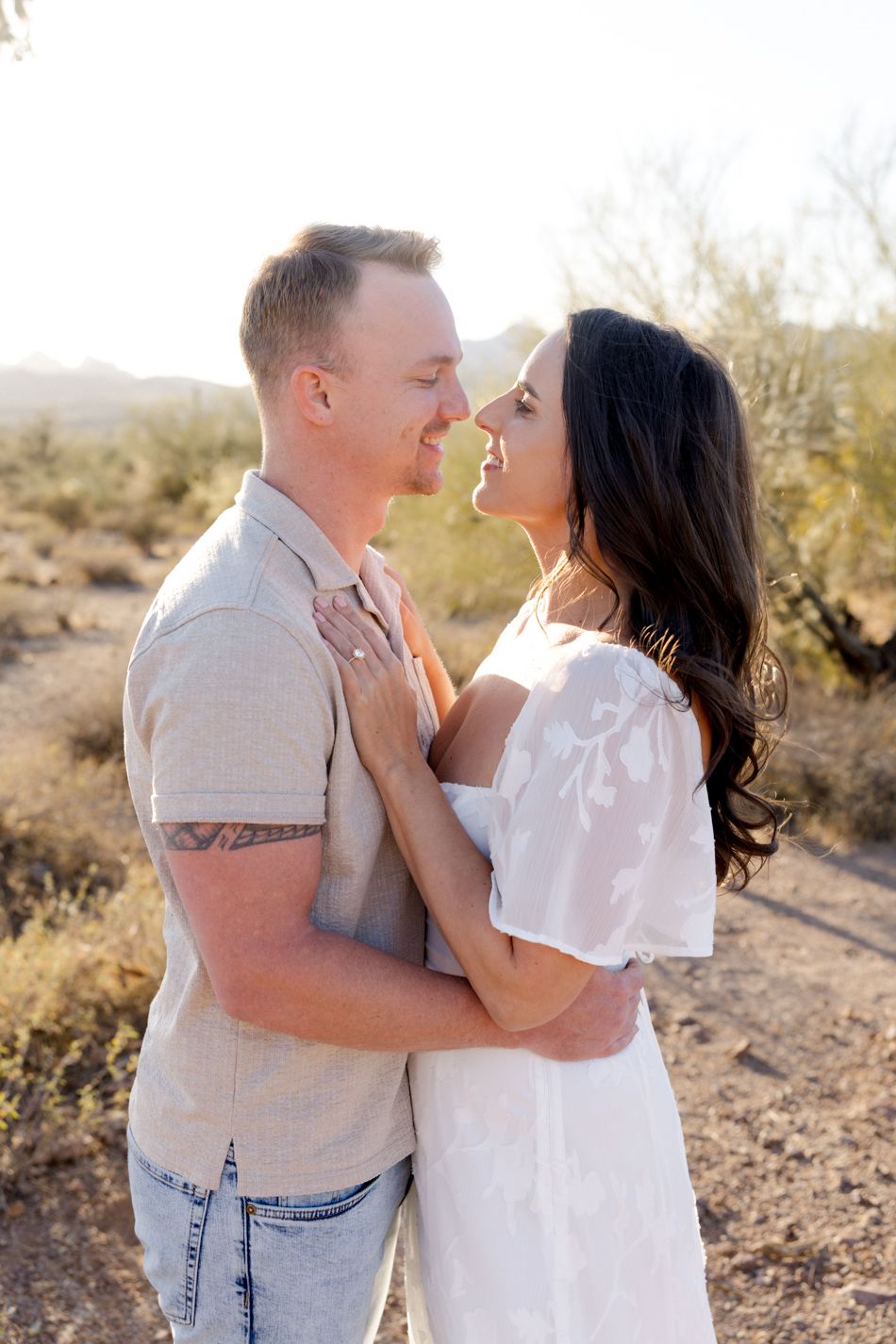 A couple embraces and poses together in a romantic desert photoshoot at sunset with desert vegetation in the background.