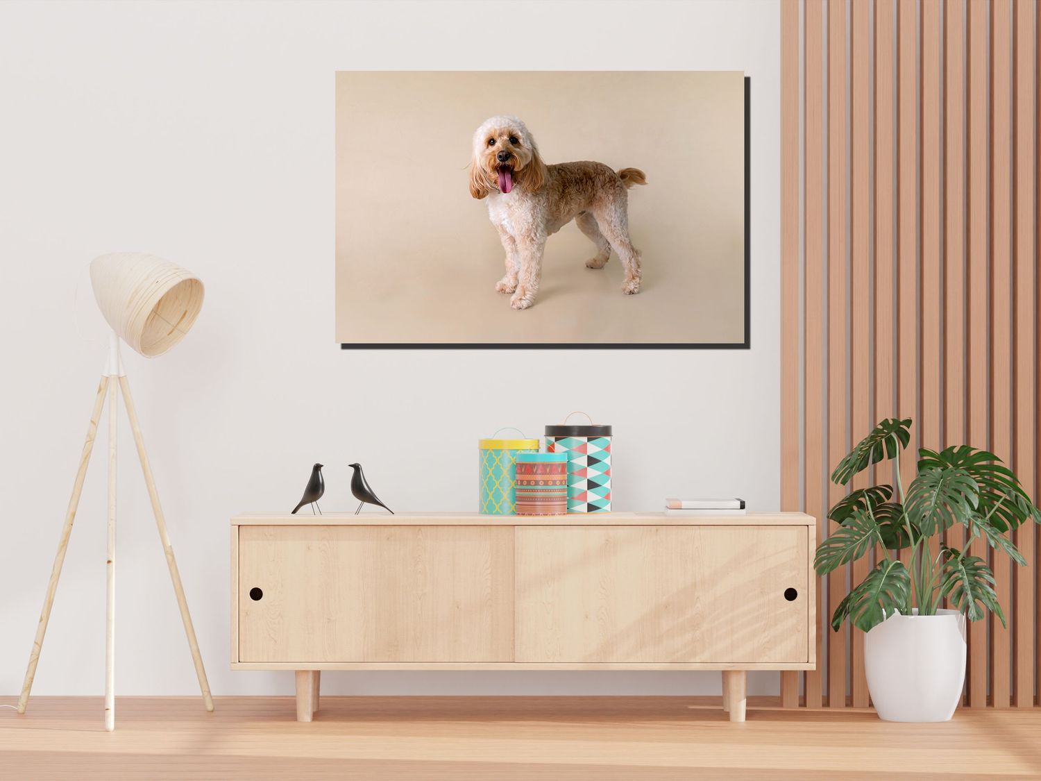 Modern living room interior with wooden credenza, floor lamp, potted plant and large dog portrait on beige wall.
