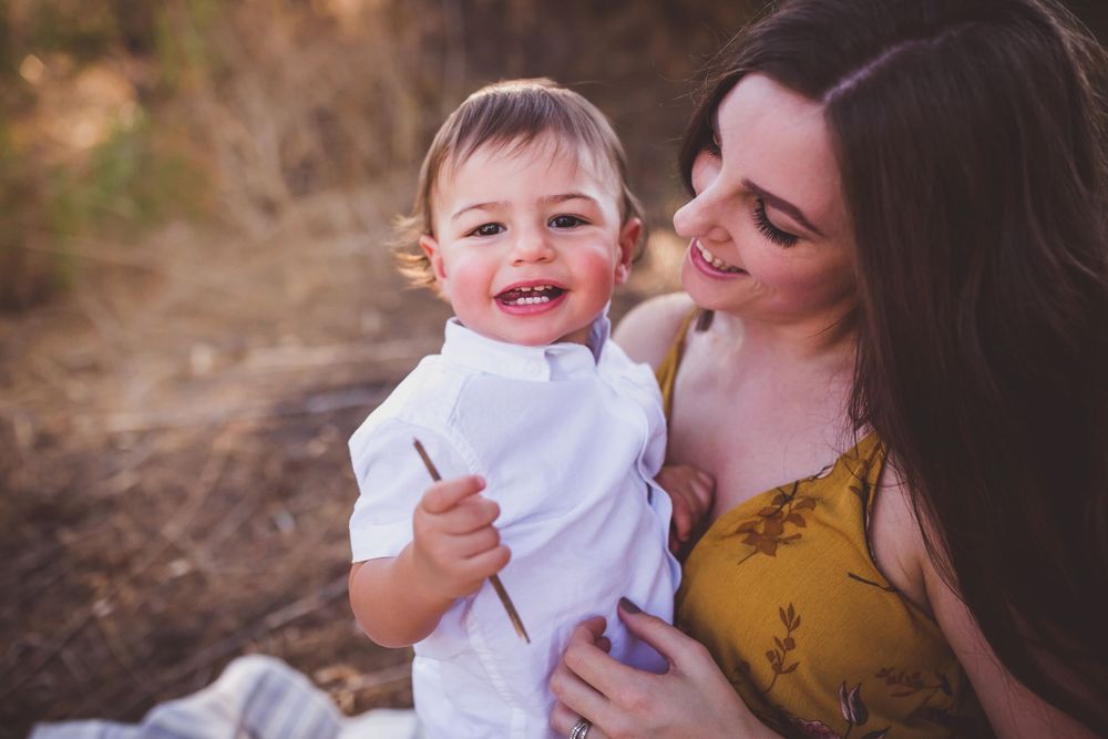 A joyful parent and infant share a tender moment outdoors during a sunset photo session.
