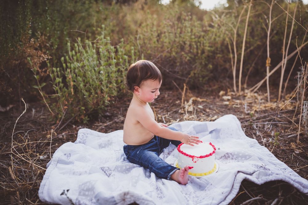 A child sits on white fabric creating colorful smears and patterns during an outdoor paint play session.