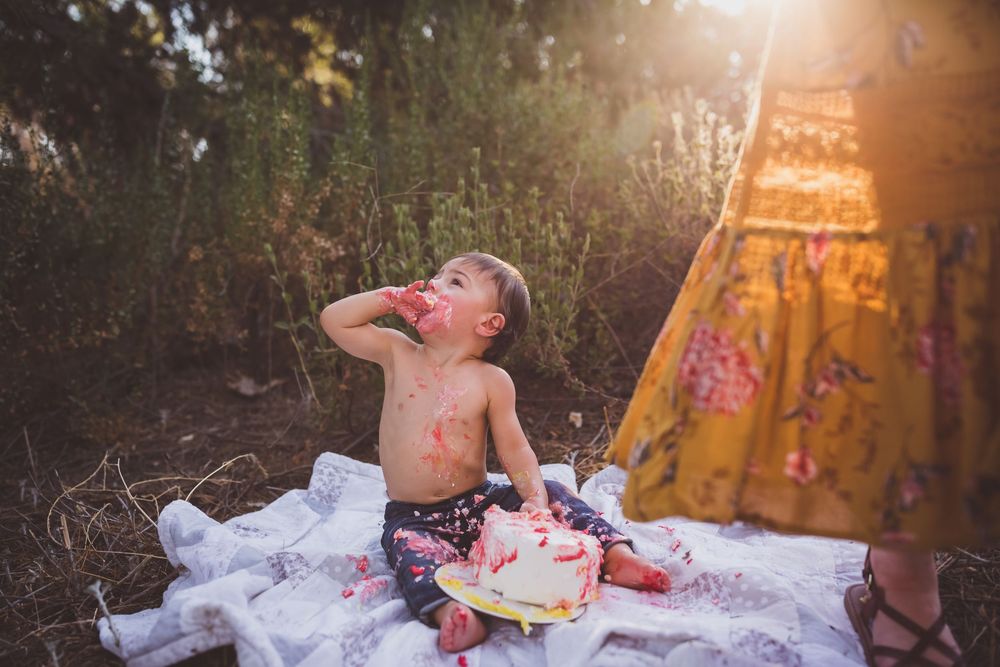 Young child enjoying an ice cream cone while sitting on a picnic blanket during a sunny summer day in nature.