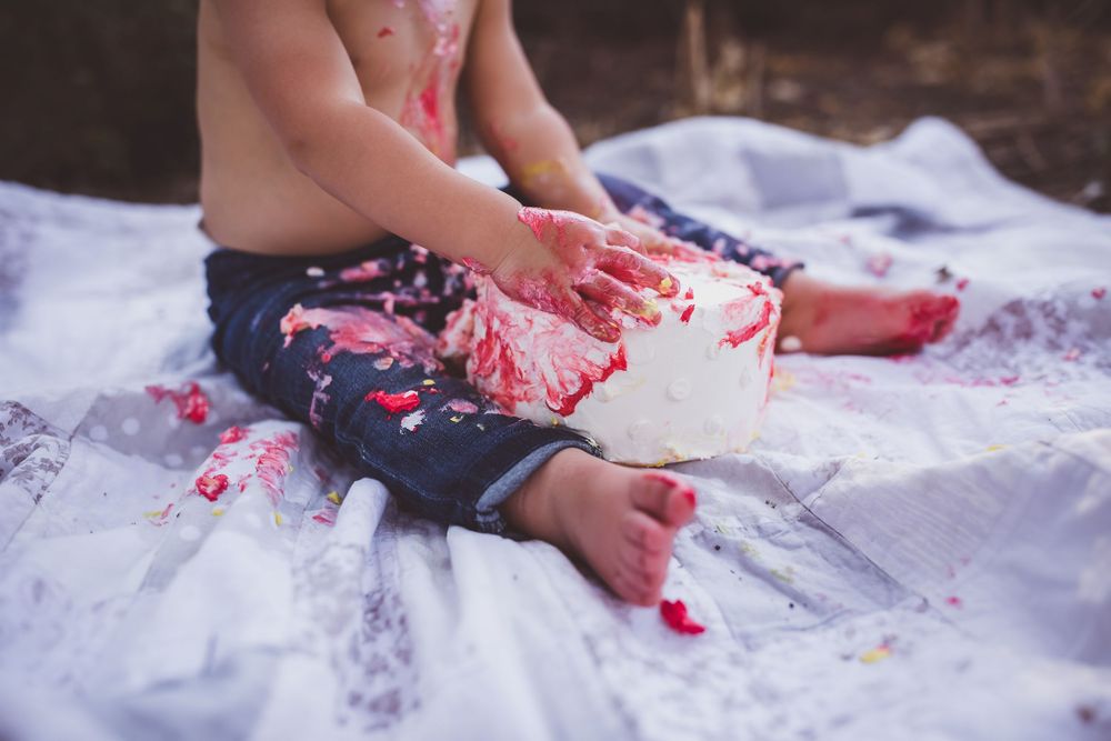 Child plays with red paint on white fabric outdoors, creating messy artistic expressions in nature.