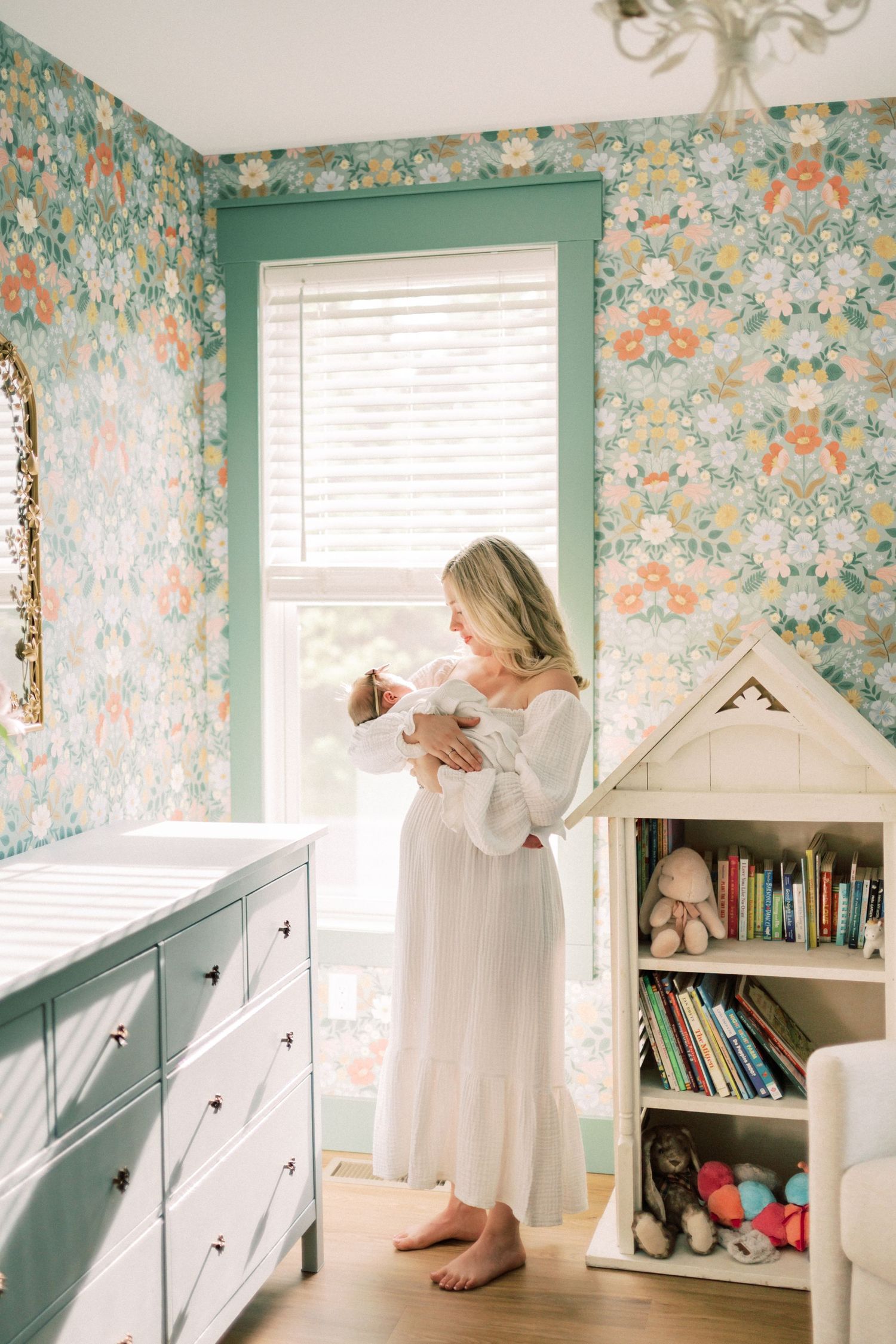 A cozy nursery with floral wallpaper features built-in storage, white trim, and natural lighting through a green-framed window.