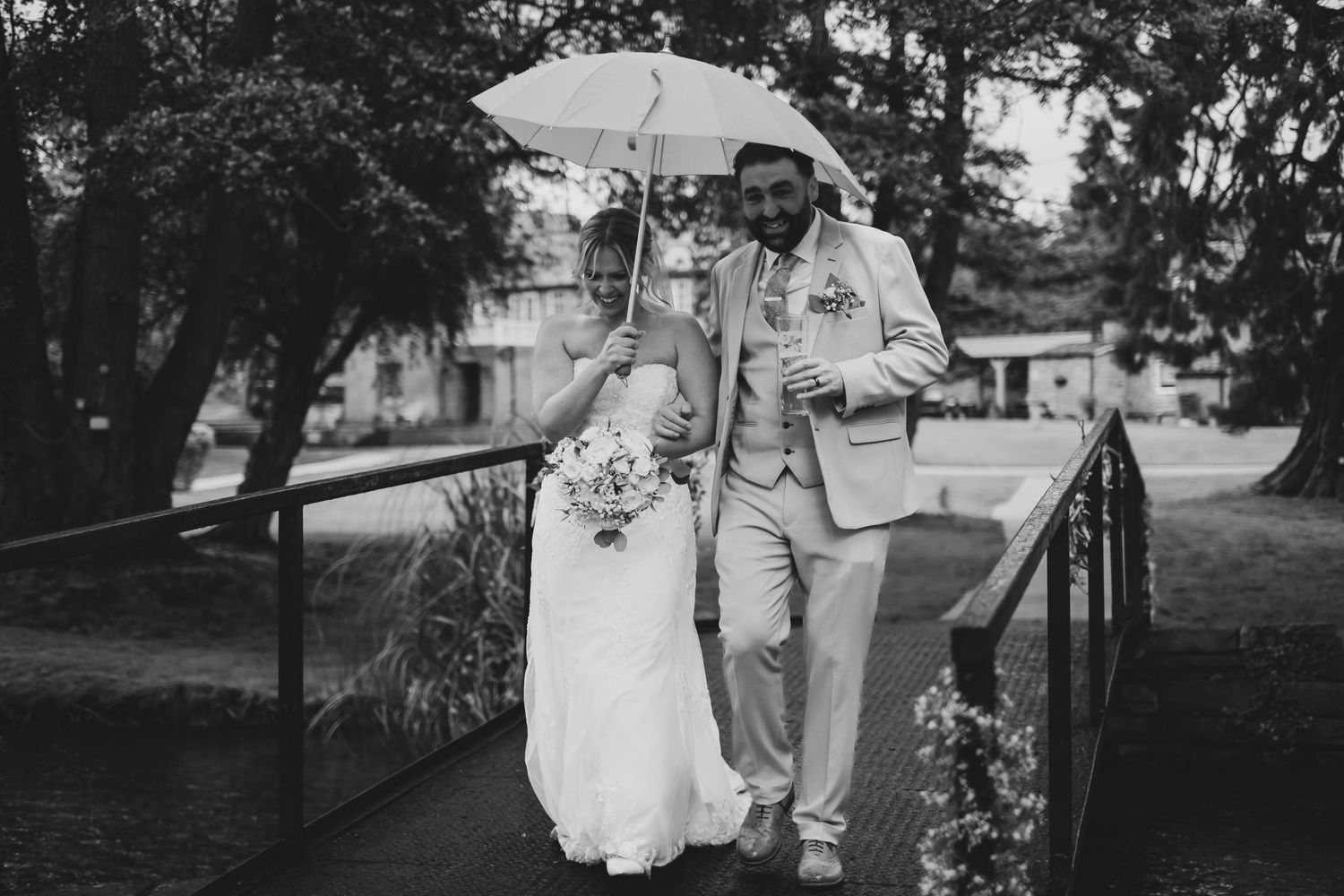 Bride and groom walking in the rain across a bridge with their umbrella