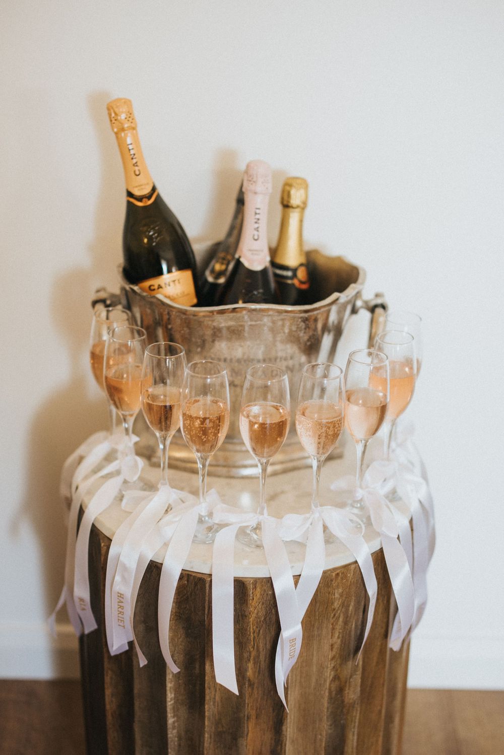 Champagne bottles chilling in an ice bucket with elegant flute glasses arranged around a rustic wooden pillar with white ribbons.
