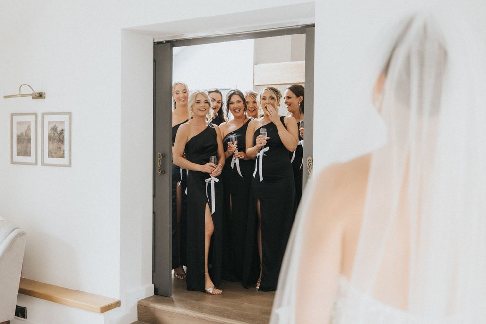 Wedding party in elegant black gowns gather around a doorway during a ceremony preparation.