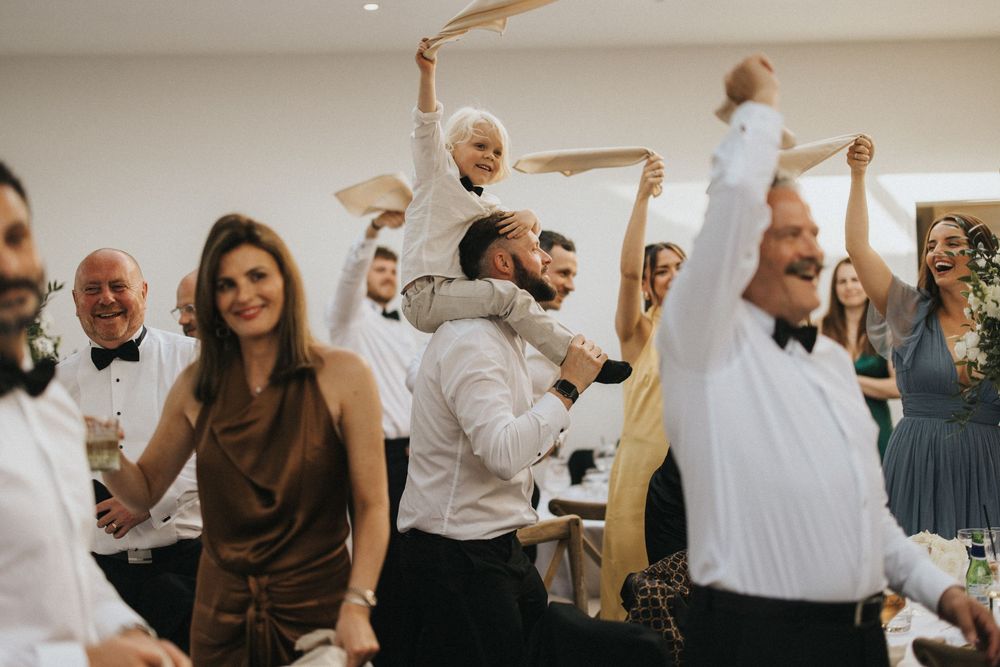 Wedding guests dance and celebrate with their napkins raised in the air during a joyous reception celebration.