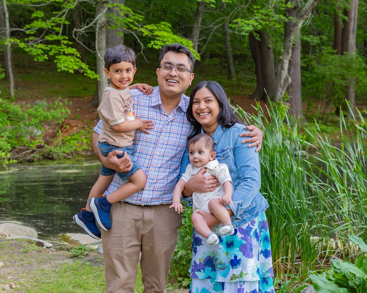 A family poses together outdoors in a series of casual portraits by a scenic lake with lush greenery in the background.