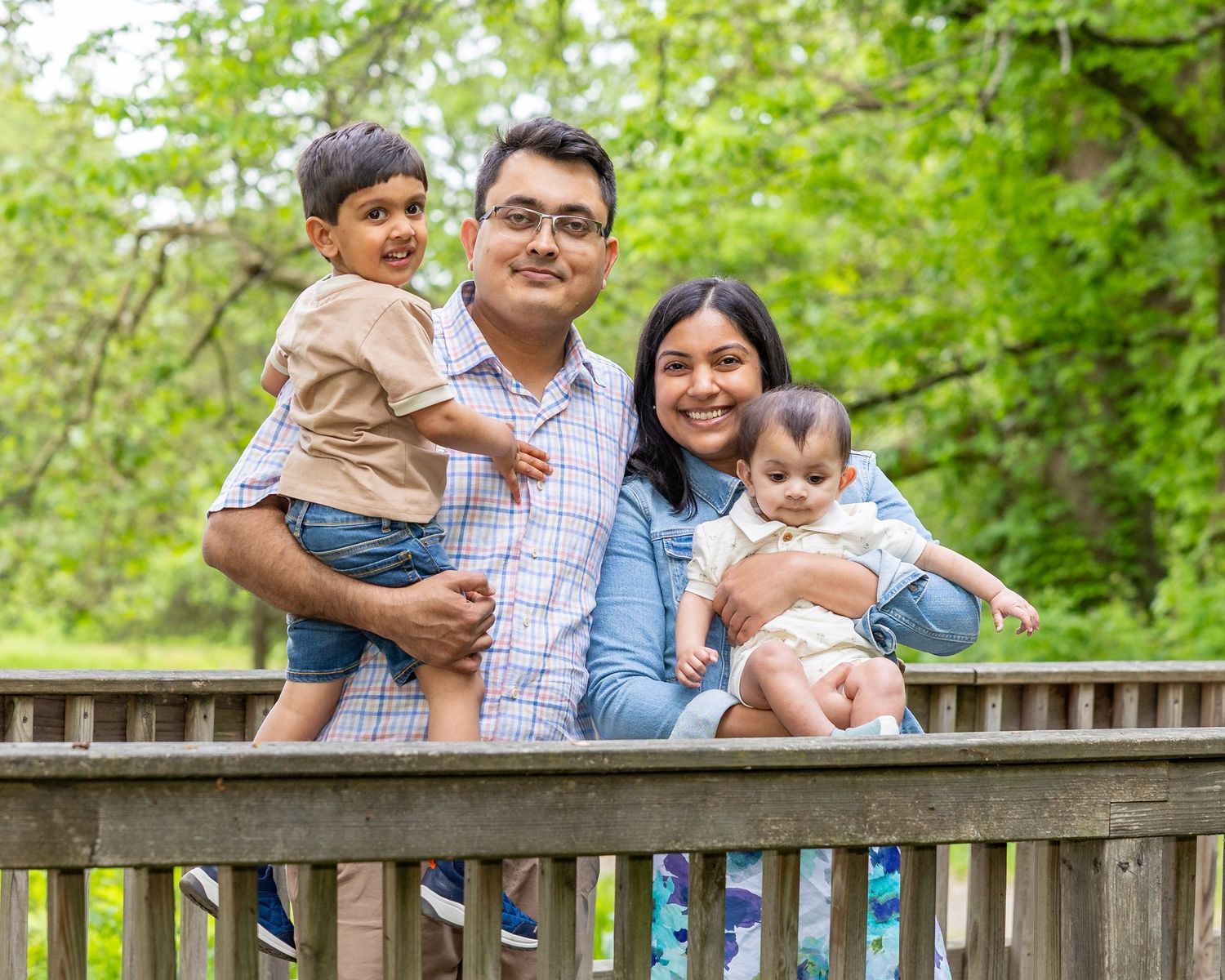 A family sits together on a wooden bench in a lush green park setting during a spring photo session.
