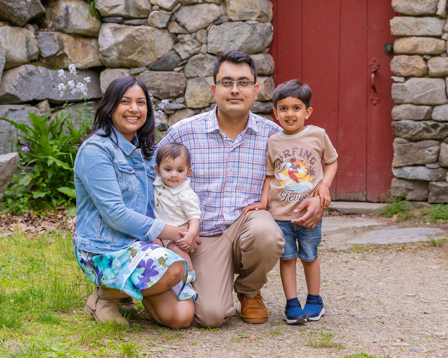 A family poses together for an outdoor portrait in front of a rustic stone wall and red wooden door.