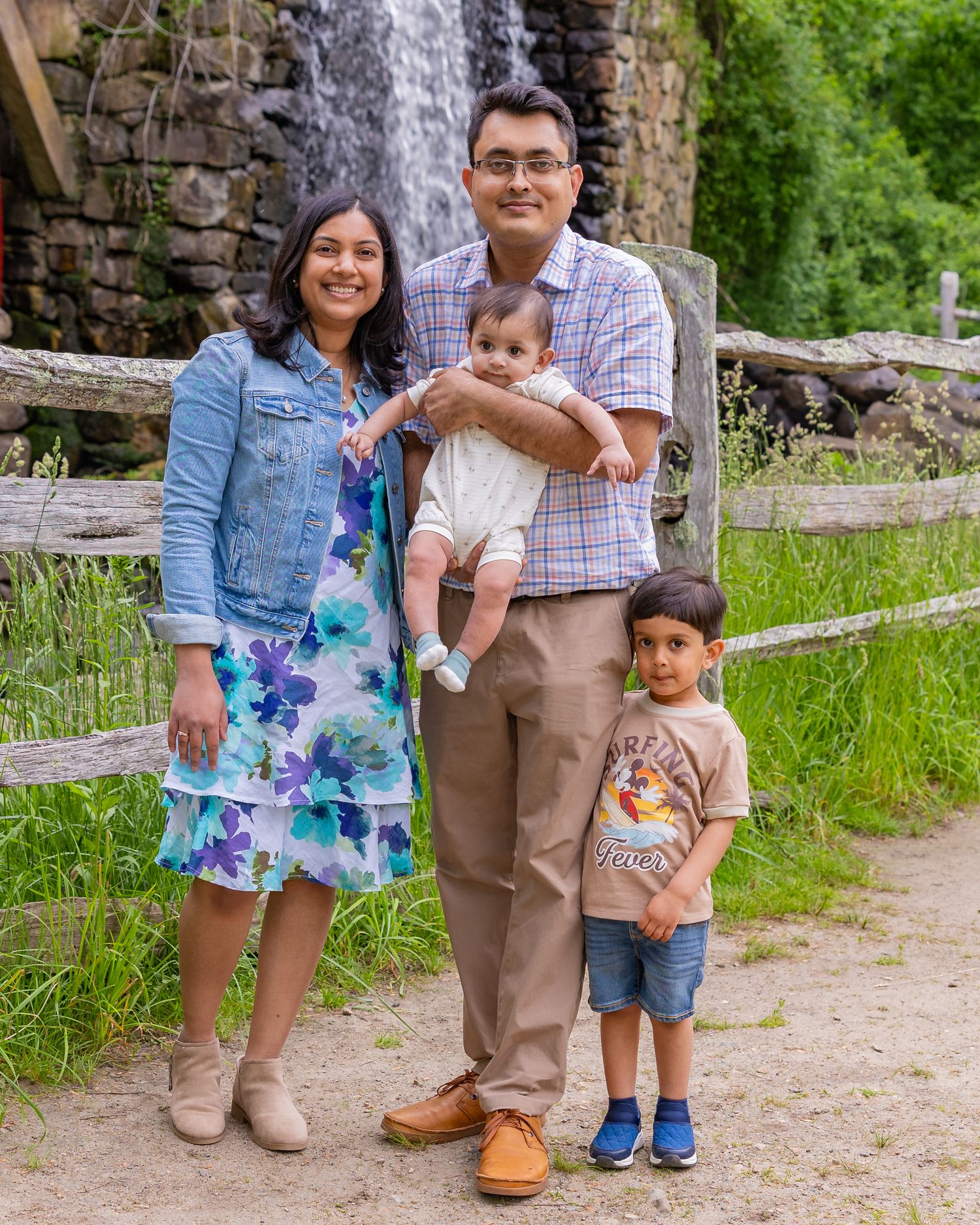 Family standing together on a rustic path surrounded by stone walls and green foliage in summer weather.