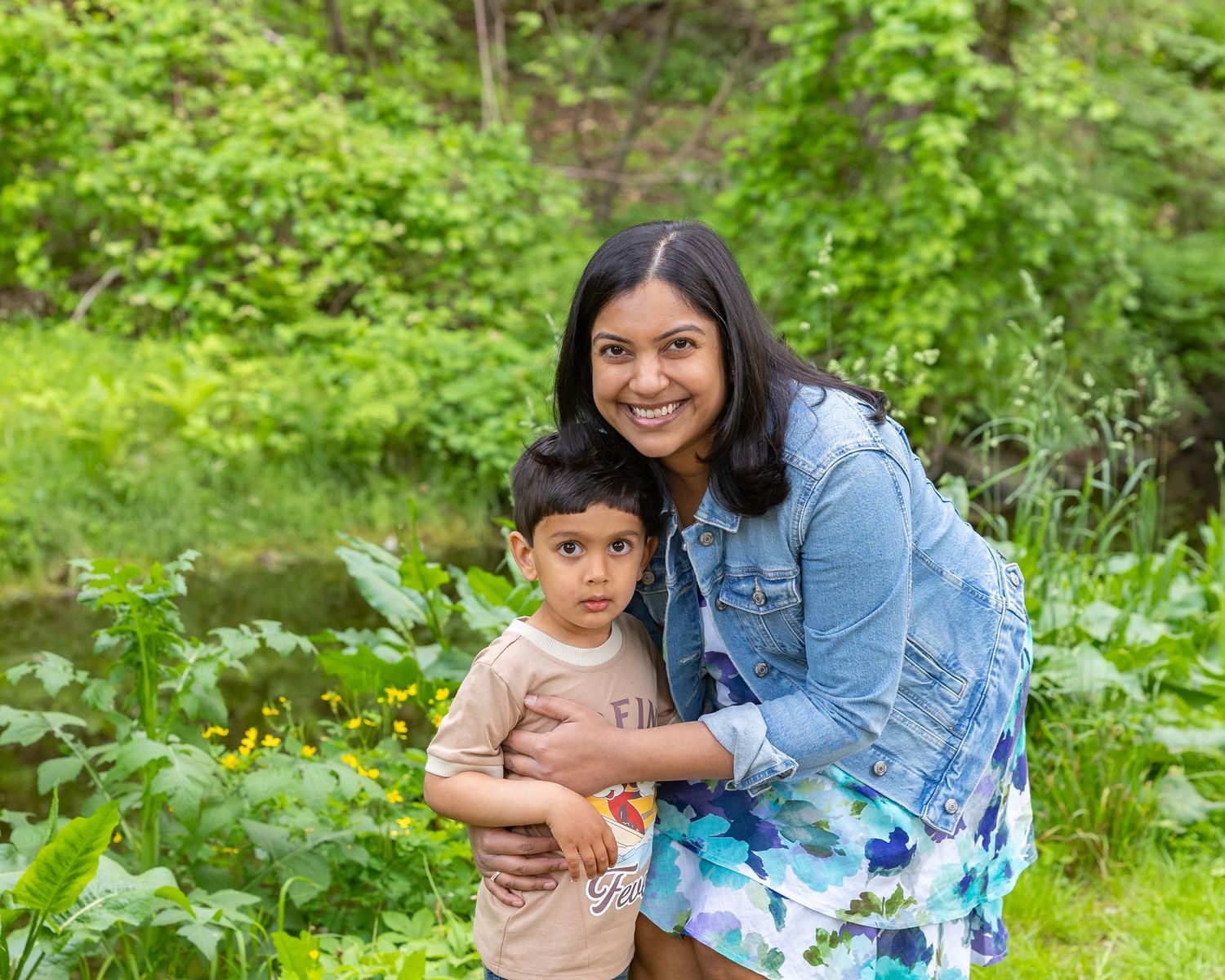 Two people in casual attire share joyful moments while posing together amid lush greenery outdoors.