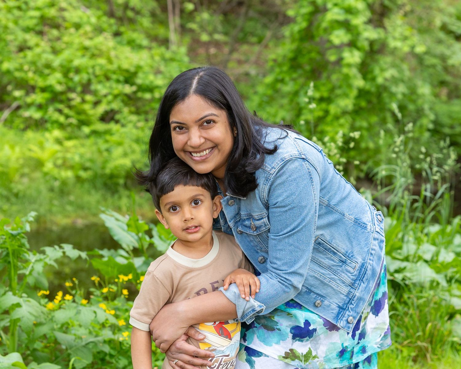 Two people in blue denim sit together outdoors surrounded by lush green foliage on a summer day.