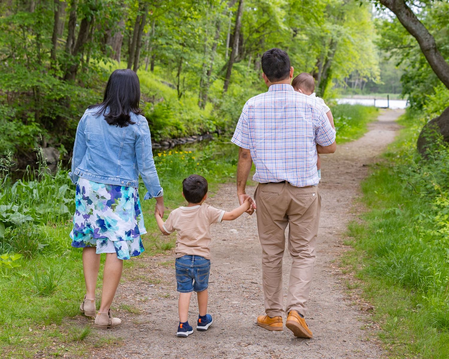 People walking together on a nature trail surrounded by lush green trees and foliage on a summer day.