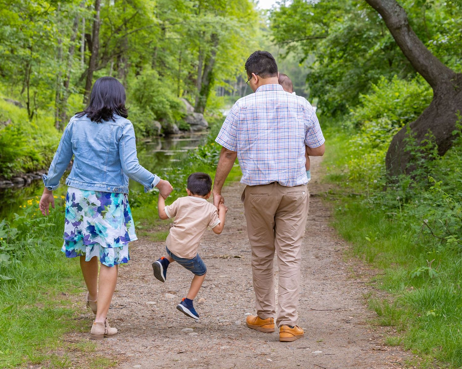 Family takes a walk together holding hands on a wooded nature trail during a sunny summer day.