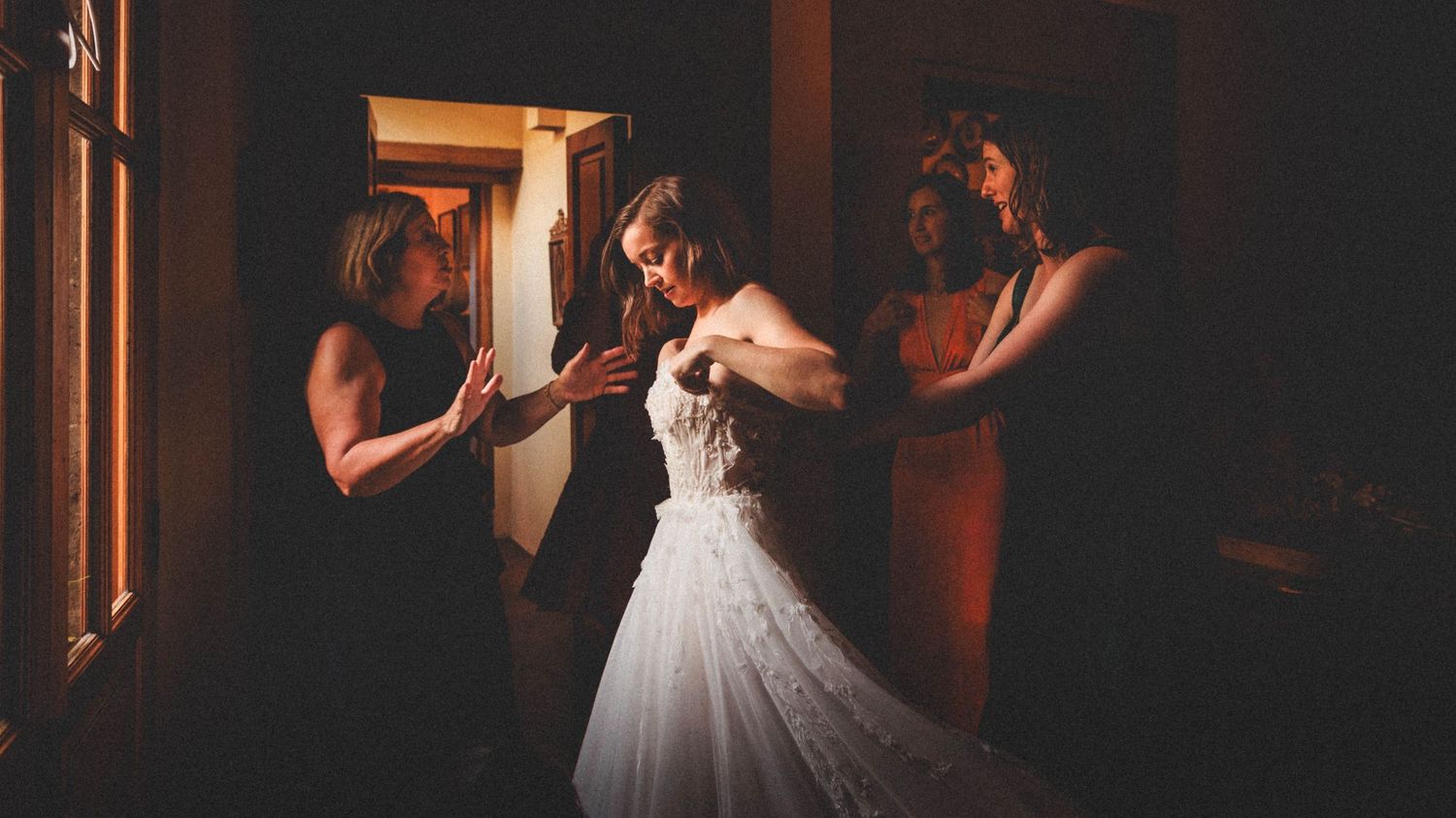 Interior wedding preparation scene with natural window lighting and white bridal gown.