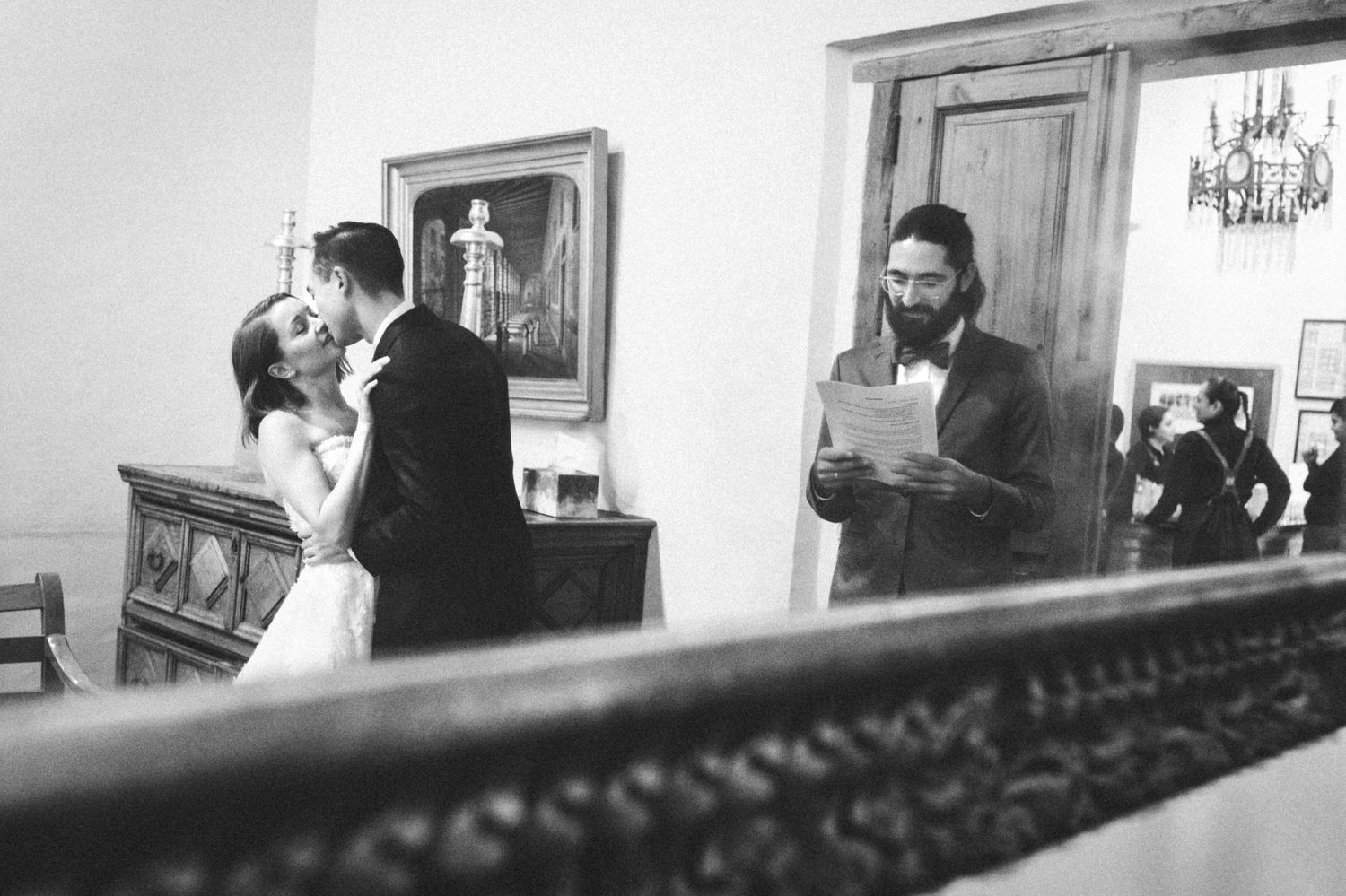 A black and white wedding ceremony moment captured through an ornate mirror frame.