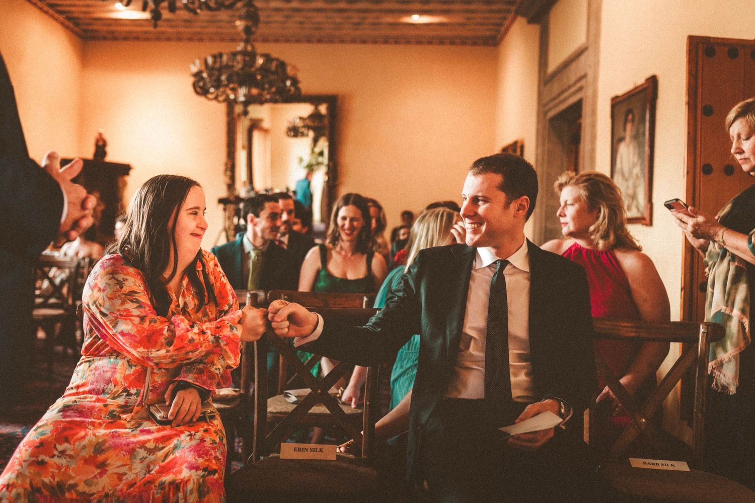 Wedding guests enjoying a lively celebration in a warmly lit room with chandeliers.