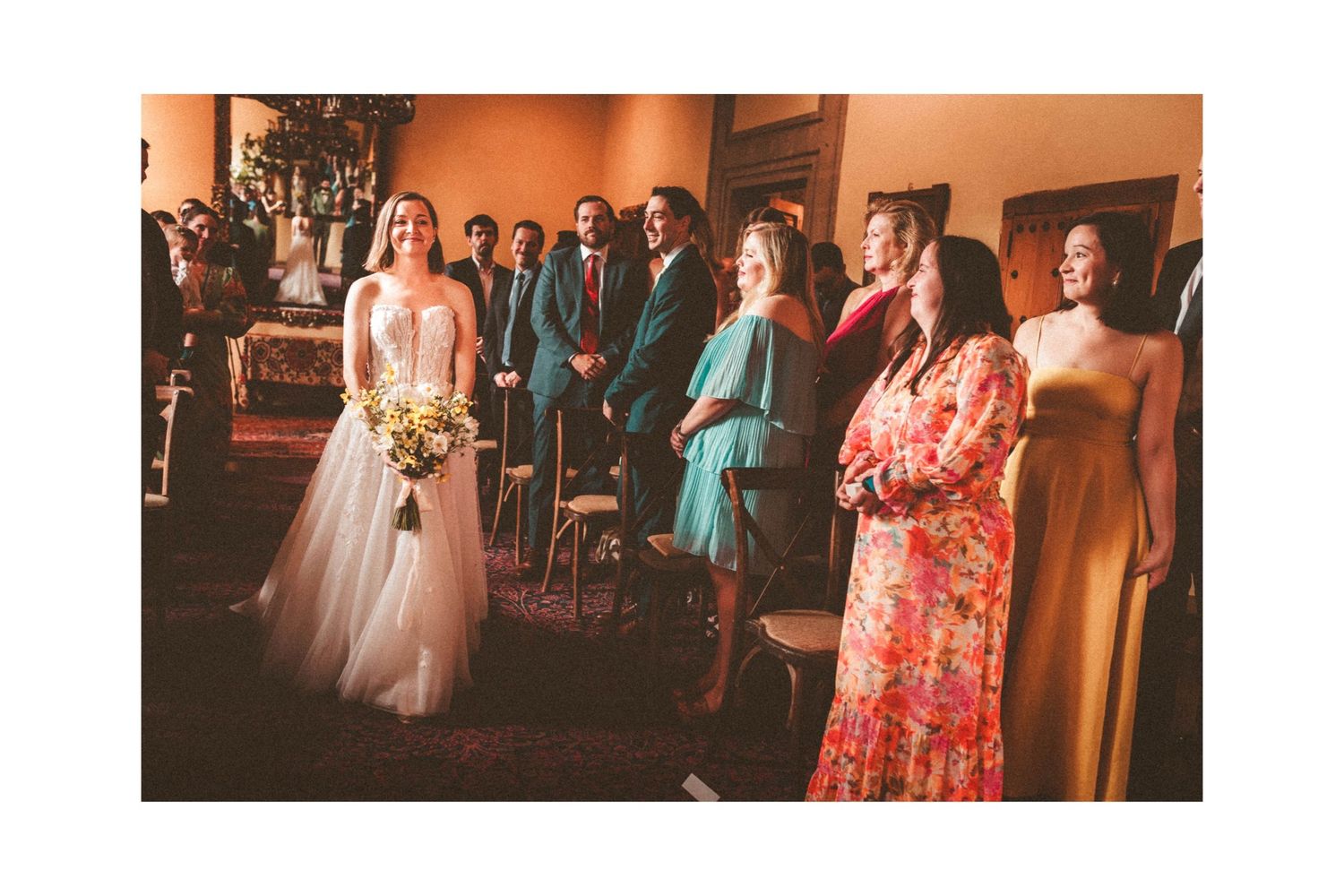 Wedding party gathered in formal attire against a peach-colored wall.