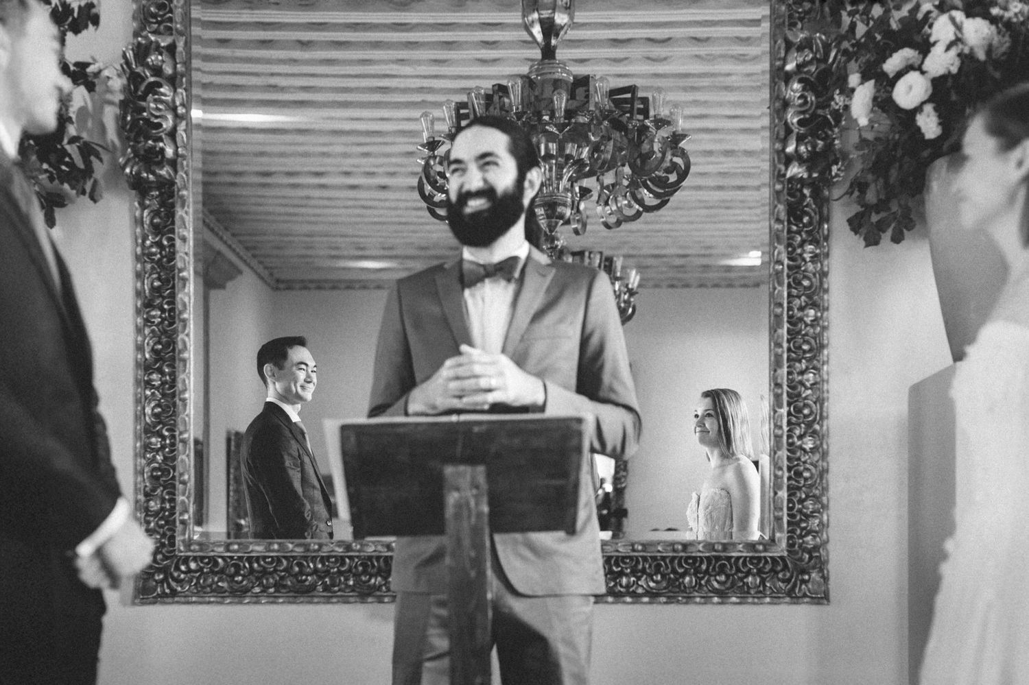 Elegant black and white wedding ceremony photo framed by decorative mirror.