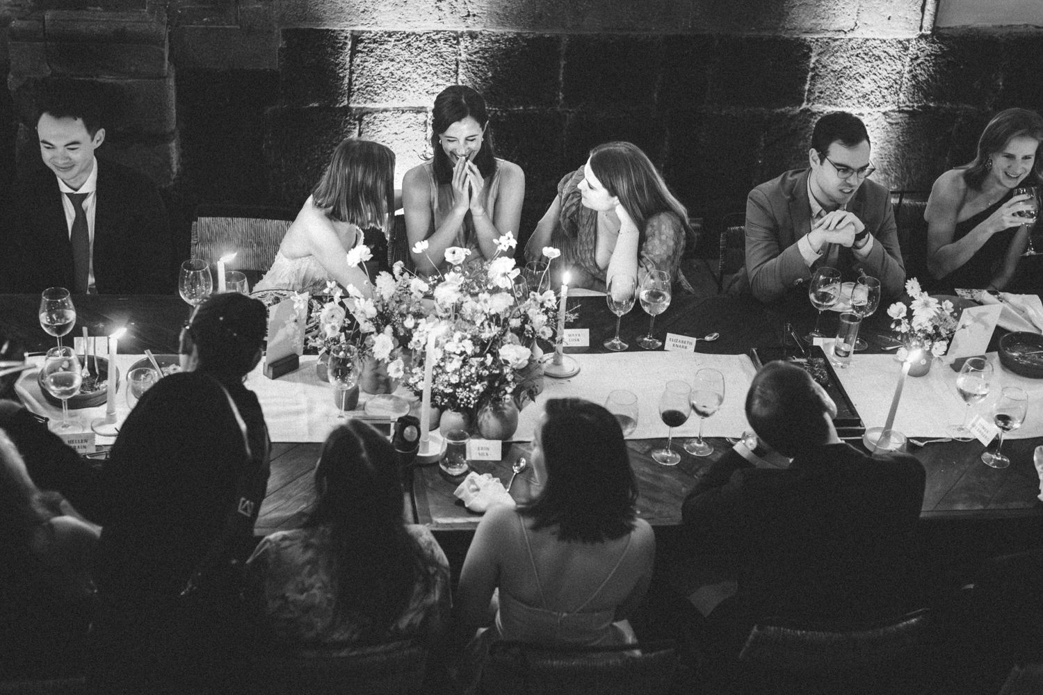 Wedding reception guests seated at long tables in a rustic stone-walled venue.