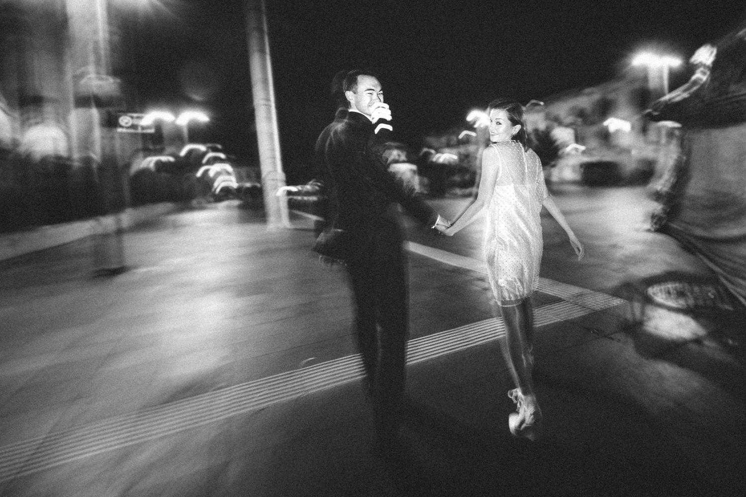 Artistic black and white photo of party guests moving through a dimly lit space.