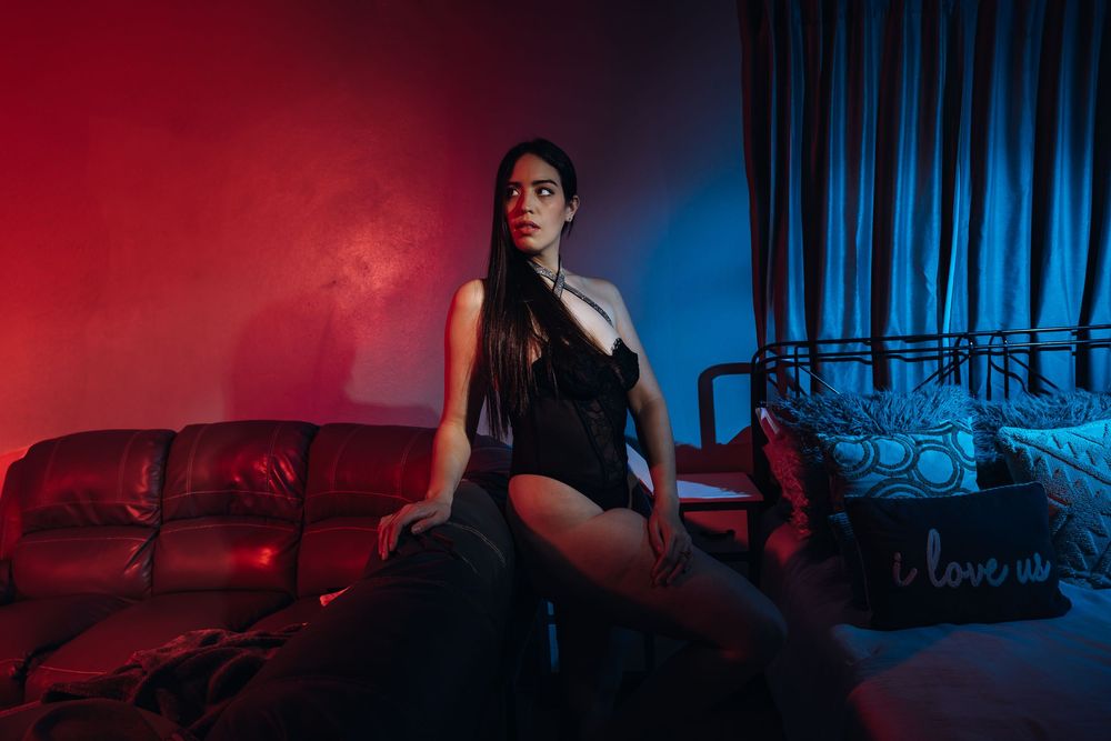 Stylish figure sits on red couch in dramatic lighting with red and blue contrasting backdrop.